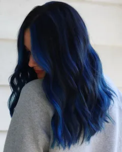 A model wearing a black and blue wig styled with loose waves and pastel highlights