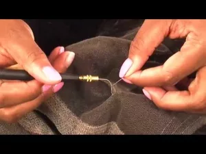 A close-up of someone stitching a torn lace wig with a needle and thread, carefully repairing the lace.