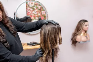 A person applying deep conditioner to a human hair wig, emphasizing the importance of regular care to maintain its quality.