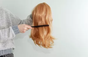 A person holding a wig securely at the base while gently brushing it with a wide-tooth comb.